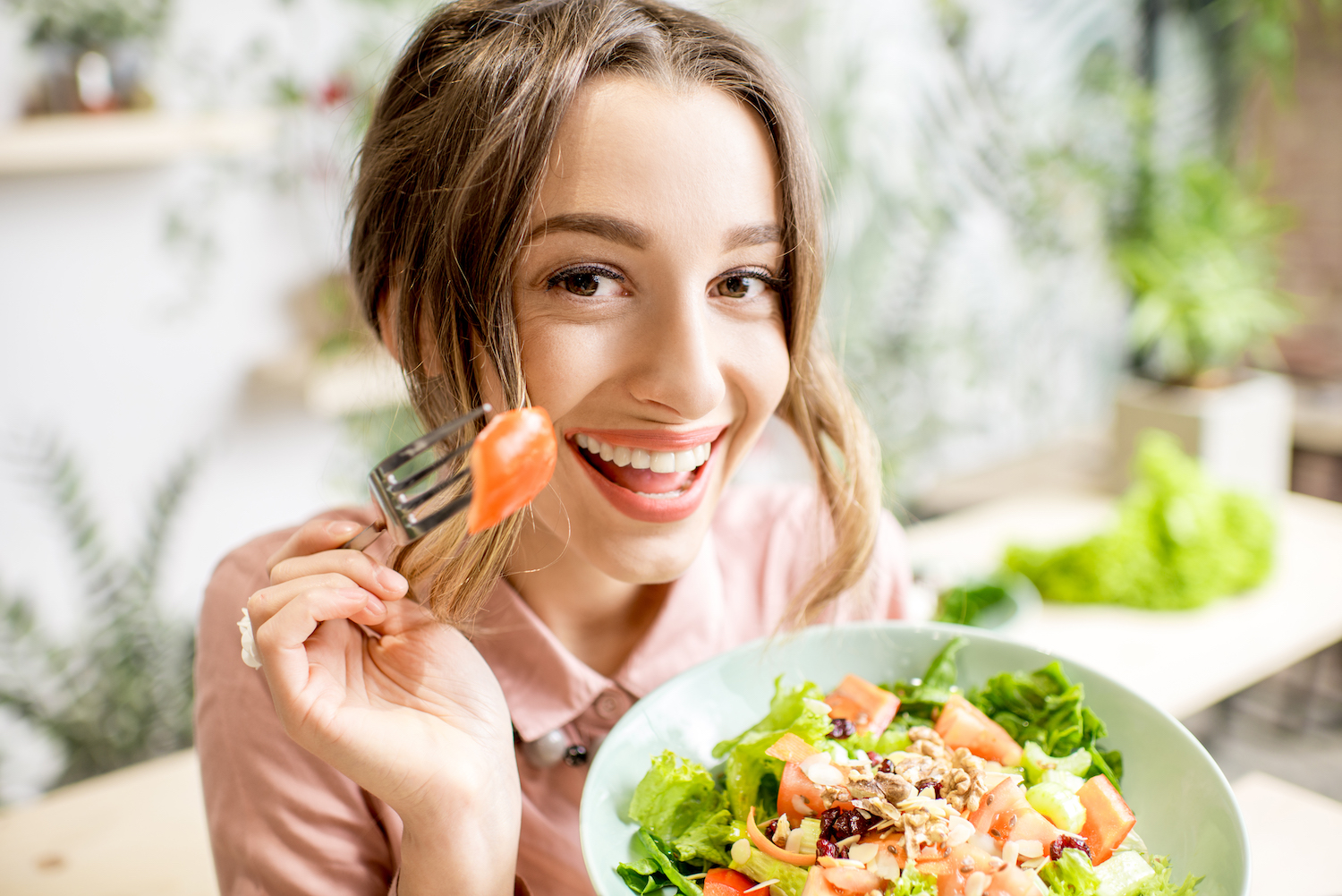 Young and playful woman eating healthy food sitting indoors on the green background